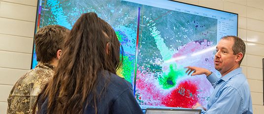 Two students and a professor looking at a radar map of the weather at South Dakota Mines.